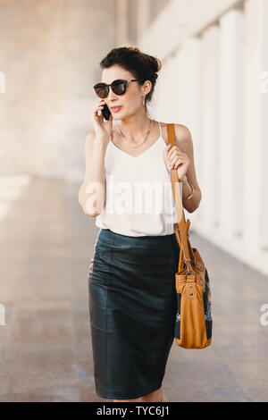 La squisita business donna in pelle gonna e camicia di seta a parlare al telefono in città all'esterno. Business, comunicazione, tecnologia e persone concep Foto Stock