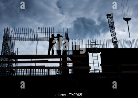 Silhouette di due lavoratori sulla parte superiore di un edificio in costruzione Foto Stock