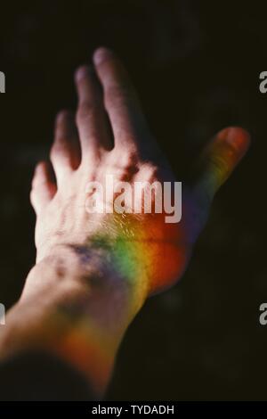 Mano di un maschio con una texture arcobaleno sul lato con uno sfondo nero Foto Stock