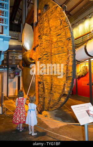 Due ragazze / Bambini bambini kid visitatori turisti guardano al timone, sollevamento del telaio & elica del SS Gran Bretagna all'interno del Dockyard Museum a Brunel della nave a vapore in Bristol. Regno Unito (109) Foto Stock