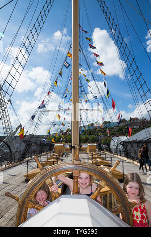 Le tre sorelle giovani ragazze pratica sterzo delle navi in legno ruota sul primario ponte superiore del SS Gran Bretagna, Brunel's Steam alimentato nave nel bacino di carenaggio. La nave è ora un museo attrazione di Bristol. Regno Unito (109) Foto Stock