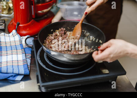 Lo chef arrosti di carne macinata in una padella profonda. Pronto ripieno con le cipolle in una ciotola sullo sfondo di spezie e verdure. Mescolare la carne fritta con un woode Foto Stock