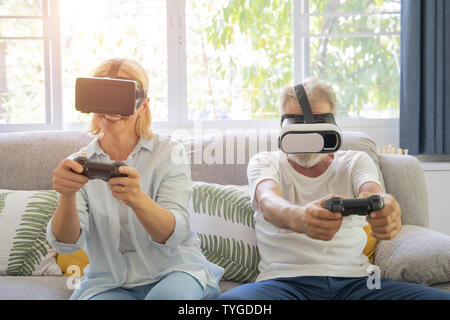 Due anziani gioiosa la riproduzione di video giochi seduto su un divano. Foto Stock