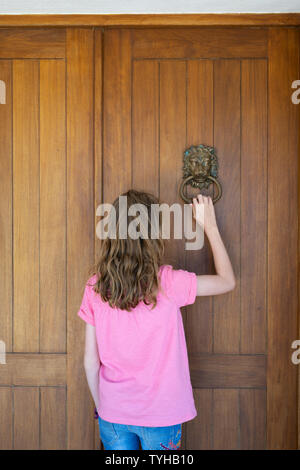 Ragazza giovane bussa alla porta anteriore di casa usando la porta di metallo respingente Foto Stock