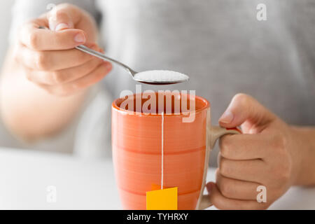 Close up di donna con aggiunta di zucchero per tazza di tè Foto Stock