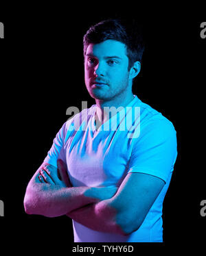 Uomo con bracci incrociati su luci al neon nelle tenebre Foto Stock