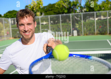 Giocatore di Tennis uomo ritratto che mostra la sfera e racket. Sorridendo felice atleta maschio che vi invitano a giocare a tennis. Attivo sano sport e fitness il concetto di stile di vita. Foto Stock