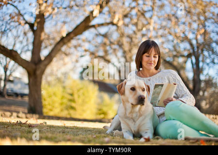 Sorridente ragazza rilassante con il suo cane e un libro in un soleggiato giardino. Foto Stock