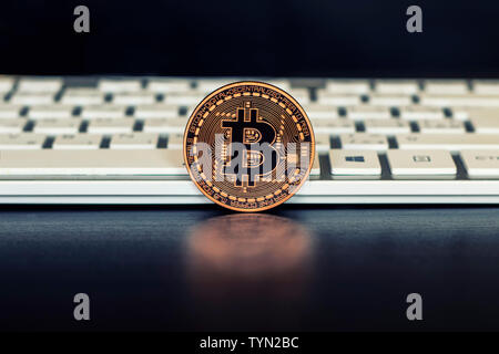 La moneta di bronzo del bitcoin sorge sullo sfondo nero nella parte anteriore delle tastiere di bianco. Bitcoin è il più noto crypto valuta. Foto Stock