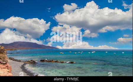 Spiaggia di pietra di Puerto de la Cruze a Isole Canarie Fuerteventura, Spagna. Ci sono acque turchesi dell'oceano e il bellissimo paesaggio con sole blu Foto Stock