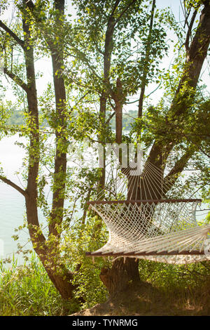 Un cotone amaca appesa tra due alberi che si affaccia su un lago e il sole è a picco buttare alberi Foto Stock