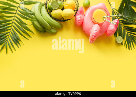 Telaio tropicale di frutti, banana, calce, foglie di palme, succo d'arancia in gommone fenicottero rosa sul pastello incalzanti sfondo giallo. Vista dall'alto. Estate essere Foto Stock