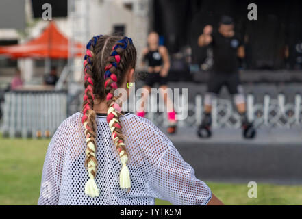 Vista posteriore di una ragazza con belle kanekalon multicolore guardando uno spettacolo di danza fuori. Foto Stock