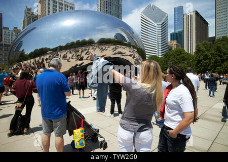 I visitatori e i turisti per il Millennium Park in una trafficata sabato mattina in estate prendere foto e selfies vicino al cloud gate bean scultura in Chicago IO Foto Stock