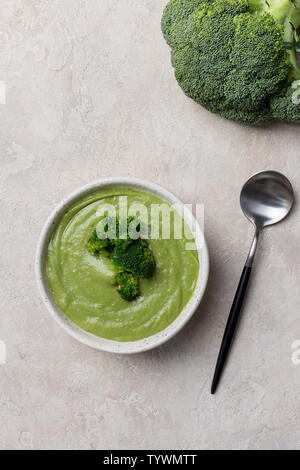 Vista sopra una gustosa minestra in crema in piatto bianco con broccoli e cucchiaio su sfondo beige. Idea di alimenti per neonati e il digiuno di persone Foto Stock