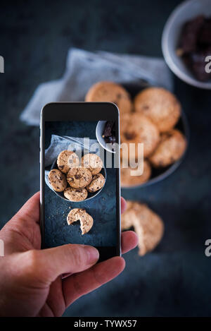 Persona di scattare una foto con un telefono per alcuni biscotti al cioccolato.i biscotti con scaglie di cioccolato e nocciole. Foto Stock