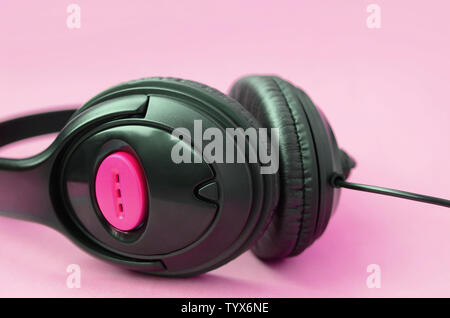 Cuffie nero giace su un pastello colorato sfondo rosa. Ascolto di musica concept Foto Stock