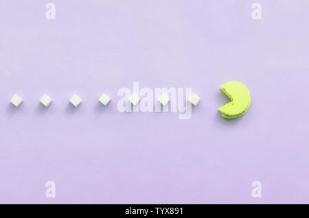 Una composizione di amaretto con una bocca aperta che sta andando a mangiare zollette di zucchero su un pastello lilla sfondo. Il concetto di vecchi video giochi. Foto Stock