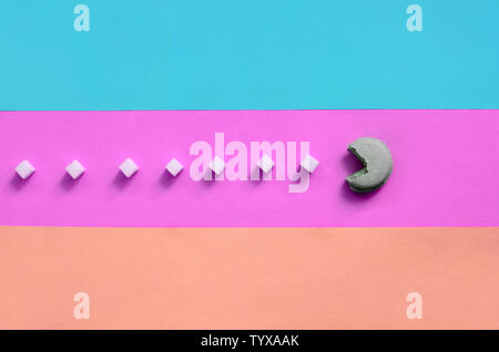 Una composizione di amaretto con una bocca aperta che sta andando a mangiare zollette di zucchero su una rosa, lime, blu e corallo sfondo color pastello. Il concetto di vecchi vi Foto Stock