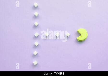 Una composizione di amaretto con una bocca aperta che sta andando a mangiare zollette di zucchero su un pastello lilla sfondo. Il concetto di vecchi video giochi. Foto Stock