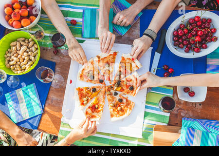Mani amiche di condividere fette di pizza da un tavolo pieno di frutti durante un dehor estivo partito. Foto Stock