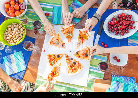 Mani amiche di condividere fette di pizza da un tavolo pieno di frutti durante un dehor estivo partito. Foto Stock