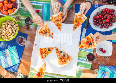 Mani amiche di condividere fette di pizza da un tavolo pieno di frutti durante un dehor estivo partito. Foto Stock