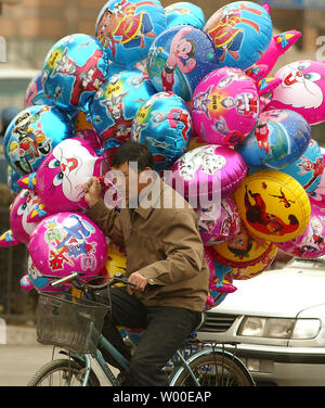 Un uomo cinese cylces con la sua palloncini attraverso un vento rigido come egli tenta di vendere palloncini con USA e giapponesi i personaggi dei cartoni animati per le strade di Pechino, Cina, Marzo 28, 2006. La Cina dovrà affrontare "gravi" sfide occupazionali questo anno e rischia di creare meno della metà dei posti di lavoro necessari per far fronte alla rapida crescita eserciti di nuove persone in cerca di lavoro e di lavoratori e lavoratrici licenziati, il paese comunista superiore della pianificazione economica ha detto in un tetro previsioni. (UPI foto/Stephen rasoio) Foto Stock