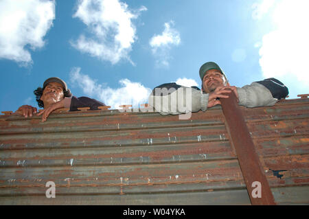 I cittadini messicani Javier Saladad (L) e Hector Guevara (R) guardare oltre il singolo recinzione che separa il Messico dagli Stati Uniti in Smugglers Gulch vicino a San Diego, California, 29 marzo 2005, durante una conferenza stampa da parte degli Stati Uniti I politici sollecitando il completamento di un periodo di quattordici miglia triple fortificato di recinzione di confine lungo il San Diego confine con Tijuana, Messico nel disprezzo per l'impatto ambientale, le specie in via di estinzione Act e altri problemi relativi alla costruzione della recinzione. (UPI foto/Earl S. Cryer) Foto Stock