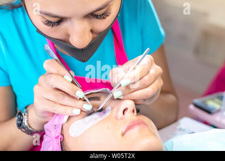 Donna master nel salone di bellezza lavoro su extension delle ciglia del cliente. Processo di lavorazione come un parrucchiere professionista per allungare le ciglia Foto Stock