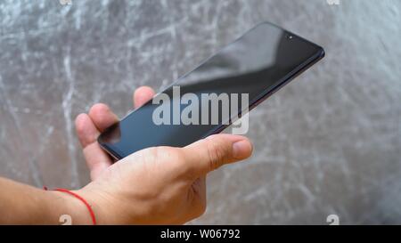 Uomo con Huawei Mate 20 X smartphone in una mano e mostrando il suo display luminoso su sfondo grigio. Studio luce lampeggia sullo schermo di Kiev, Ucraina 1 Foto Stock