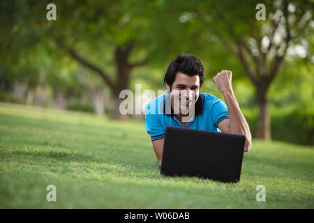 Indian giovane alzando la mano mentre utilizzando laptop in un parco Foto Stock