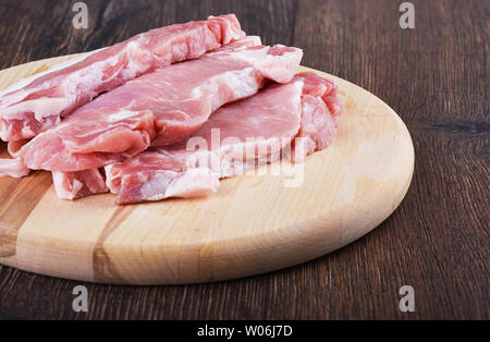 Bistecche di maiale su un tagliere di legno. Carne di maiale cruda per bistecche. Stile rustico. Foto Stock