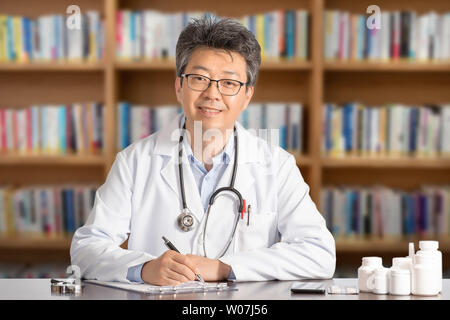 Maschio asiatici medico seduto alla scrivania sorridente. Foto Stock