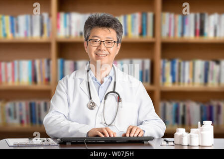 Maschio asiatici medico seduto alla scrivania sorridente. Foto Stock