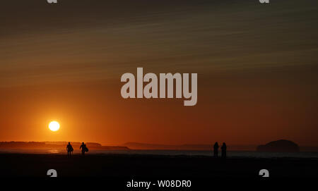 Surfisti sulla spiaggia Belhaven vicino a Dunbar in confini Scozzesi dopo il tramonto. Foto Stock