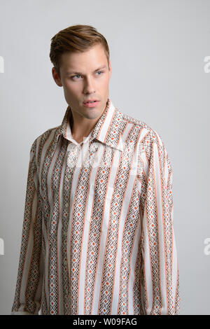 Un modello maschio caucasico di capelli marroni si pone in una camicia a strisce vintage, un editoriale di moda vintage maschile. Foto Stock