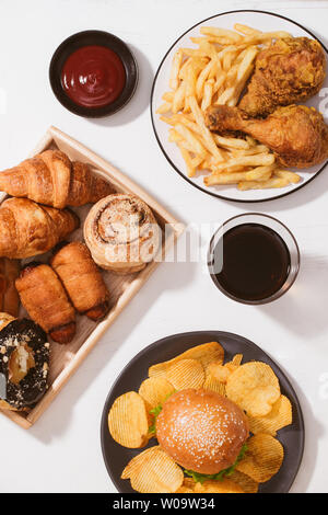 Pane appena sfornato, panini, grandi hamburger, fritto croccante di pollo e patatine fritte sul tavolo bianco - cibo malsano concetto Foto Stock