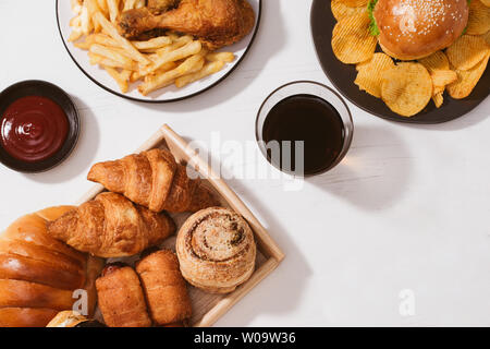 Pane appena sfornato, panini, grandi hamburger, fritto croccante di pollo e patatine fritte sul tavolo bianco - cibo malsano concetto Foto Stock