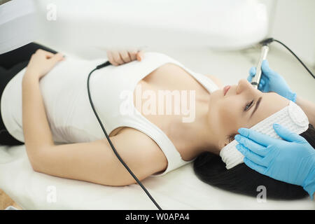 Medico con scraber ad ultrasuoni. Eseguendo la procedura di pulizia ad ultrasuoni del viso. Modello, profilo. Clinica cosmetologico. Paziente. Assistenza sanitaria e clinica Foto Stock