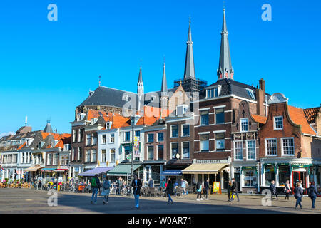 Delft, Paesi Bassi - 8 Aprile 2016: Colorful street view con case olandesi tradizionali sulla piazza, cupole della chiesa, biciclette, gente che passeggia in downtown Foto Stock