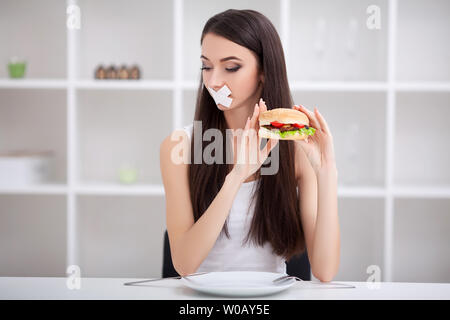 La dieta. Vicino la faccia del giovane bella triste donna latina con la bocca chiusa a tenuta su stick nastro Foto Stock