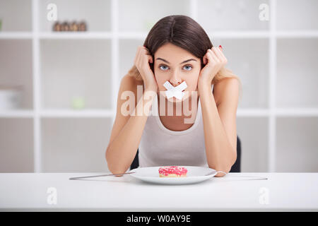 La dieta. Vicino la faccia del giovane bella triste donna latina con la bocca chiusa a tenuta su stick nastro Foto Stock