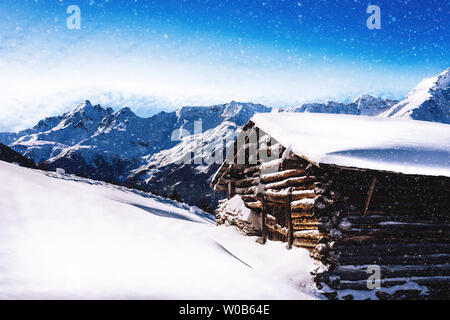 Alta altitudine chalet in legno cottage con luce di neve che cade con Alpi mountain range in background Foto Stock