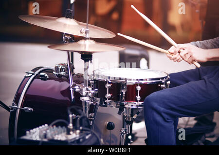 Il ragazzo è un musicista di strada in pantaloni blu suonare rhythm su un bel rosso drum set con bacchette di legno Foto Stock