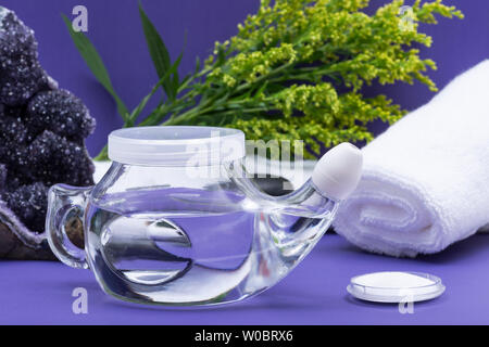 Spa sfondo viola con Neti Pot, pila di soluzione salina, arrotolato asciugamani bianchi e impilati pietre di basalto. Lavaggio del seno. Irrigazione nasale. Foto Stock