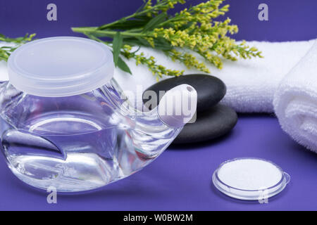 Spa sfondo viola con Neti Pot, pila di soluzione salina, arrotolato asciugamani bianchi e impilati pietre di basalto. Lavaggio del seno. Irrigazione nasale. Foto Stock