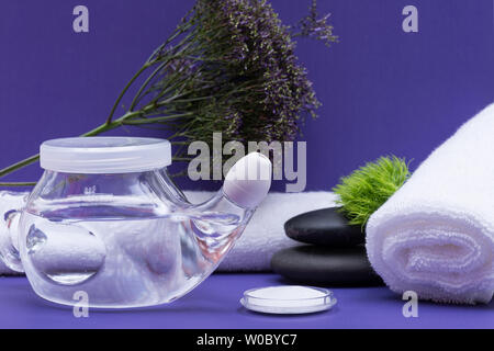 Spa sfondo viola con Neti Pot, pila di soluzione salina, arrotolato asciugamani bianchi e impilati pietre di basalto. Lavaggio del seno. Irrigazione nasale. Foto Stock