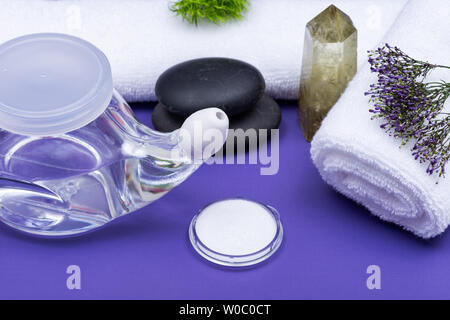 Spa sfondo viola con Neti Pot, pila di soluzione salina, arrotolato asciugamani bianchi e impilati pietre di basalto. Lavaggio del seno. Irrigazione nasale. Foto Stock