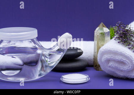 Spa sfondo viola con Neti Pot, pila di soluzione salina, arrotolato asciugamani bianchi e impilati pietre di basalto. Lavaggio del seno. Irrigazione nasale. Foto Stock